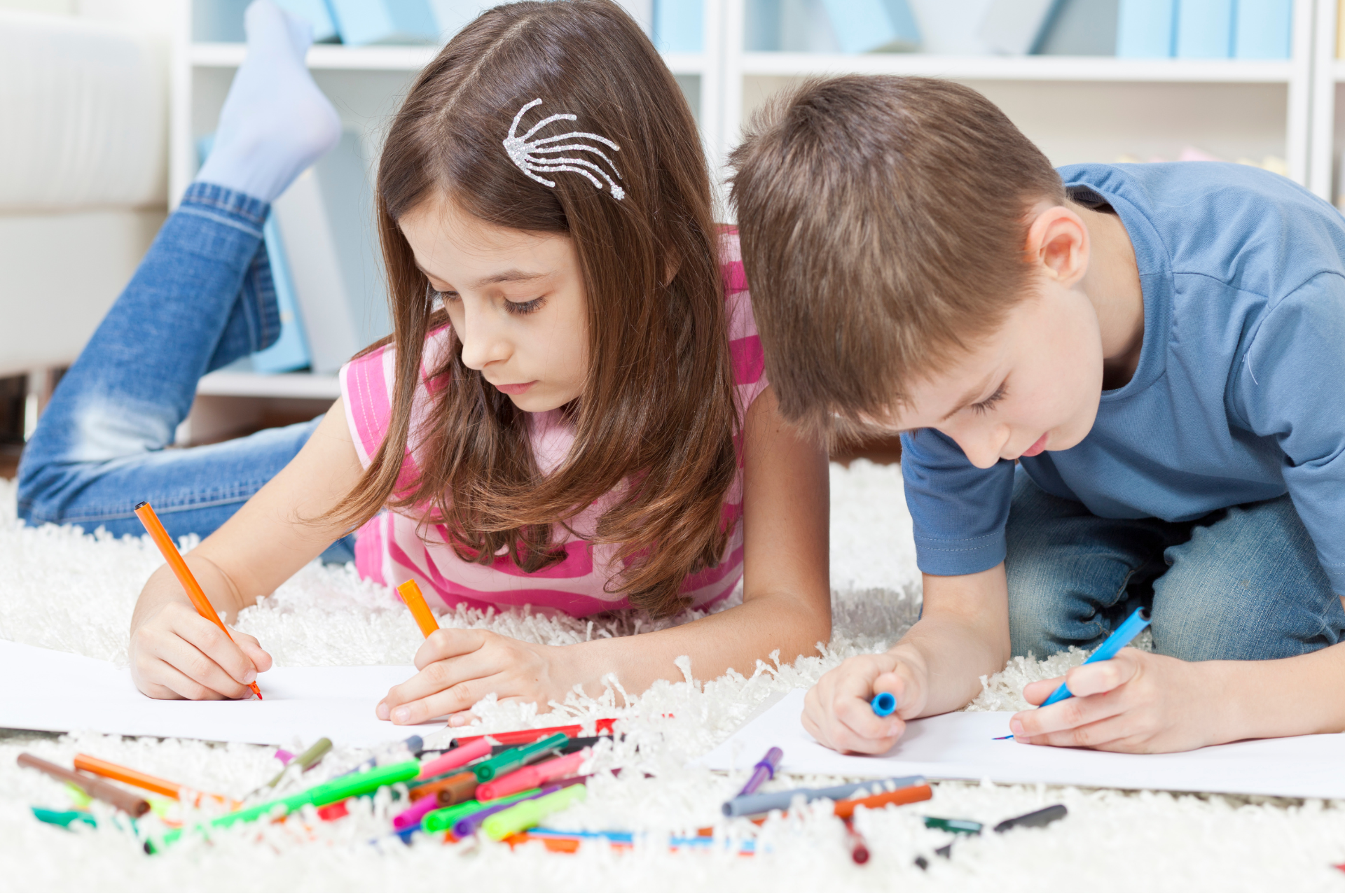 Na obrazku widzimy grupę dzieci w różnym wieku, zanurzonych w procesie tworzenia. Ich twarze są pełne skupienia, a w ich rękach trzymają kolorowe kredki i pisaki. Wokół nich rozrzucone są kartki papieru, zapełnione barwnymi rysunkami – od prostych domków i drzew, po skomplikowane sceny z kosmicznymi postaciami i fantastycznymi zwierzętami. Światło wpadające przez okno oświetla ich twórczą pracę, tworząc ciepłą i inspirującą atmosferę.